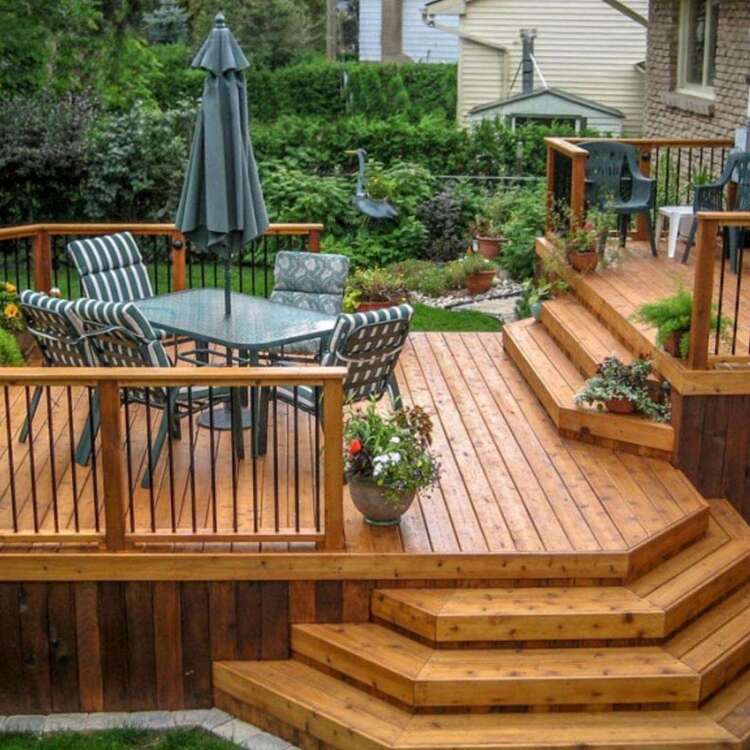 A photo of a covered deck at dusk, lit up by overhead pot lights and an outdoor stone fireplace. There is a large beige sectional, and a built-in pool.