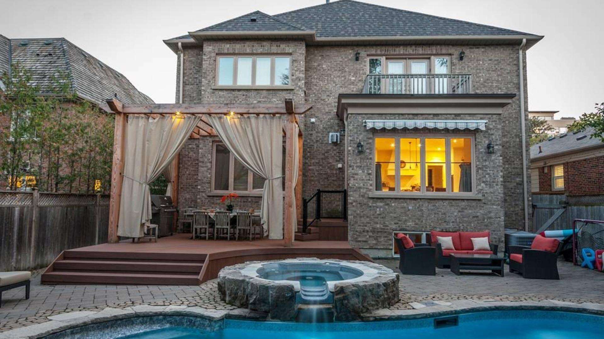 A backyard view of a modern home with a luxury pool and a gorgeous wooden deck featuring an outdoor dining and seating area