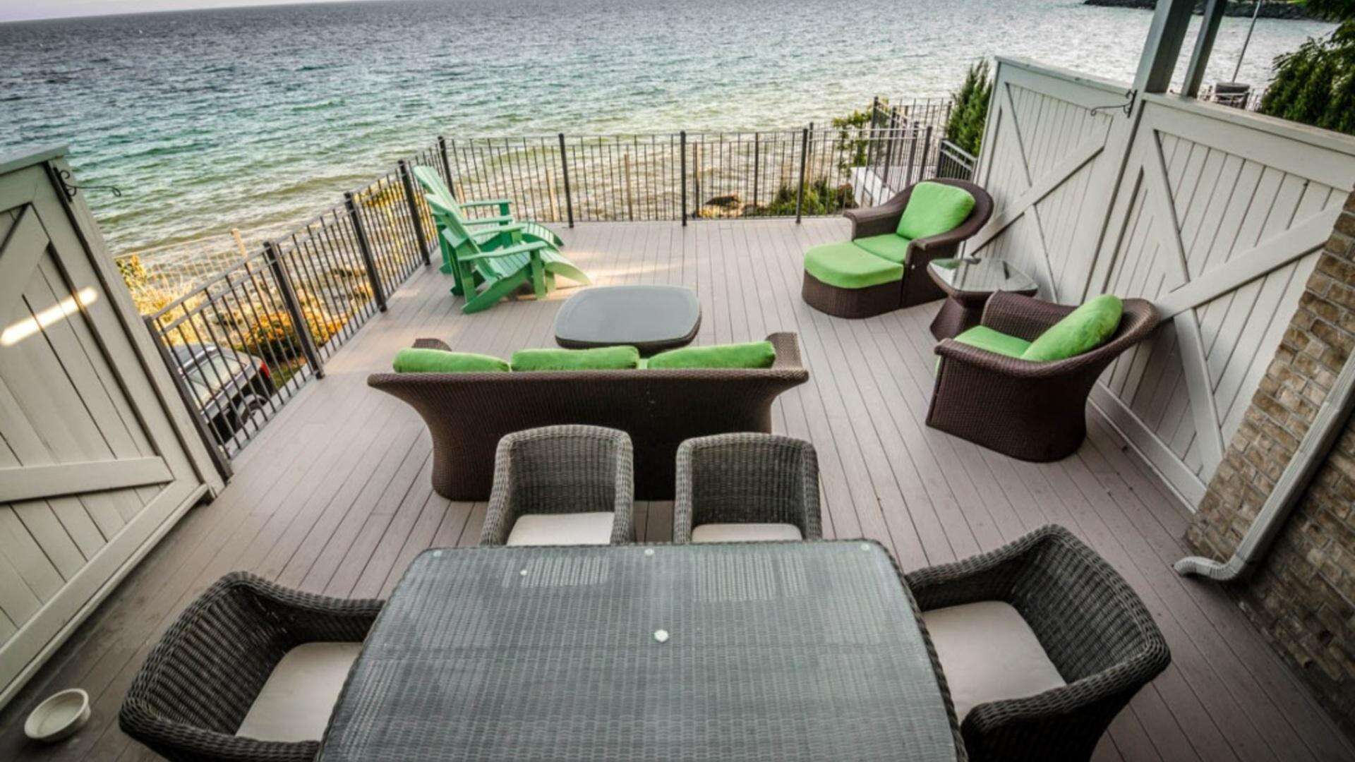 A beautiful wood finished deck overlooking the beach with green outdoor furniture