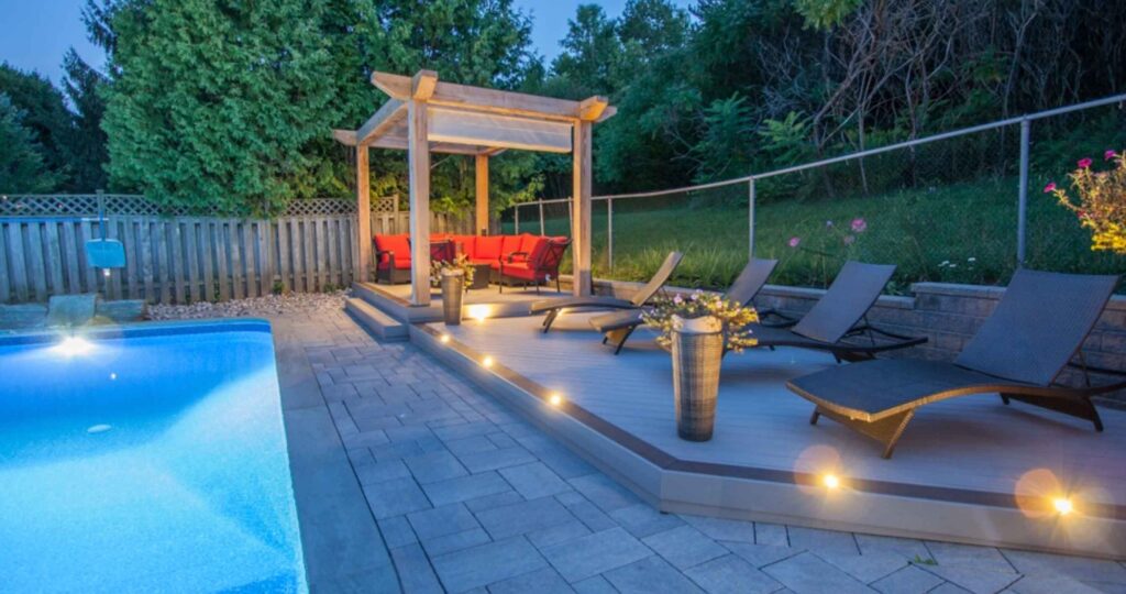 Two-level PVC deck beside a pool with a stone patio, pergola shade, and outdoor lighting