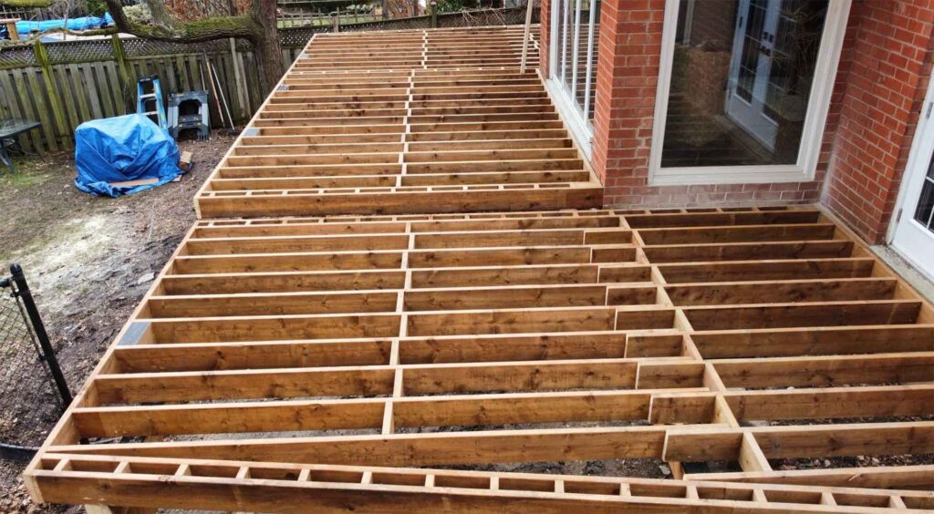Deck framing attached to a house, showing joists and structural support before decking installation.