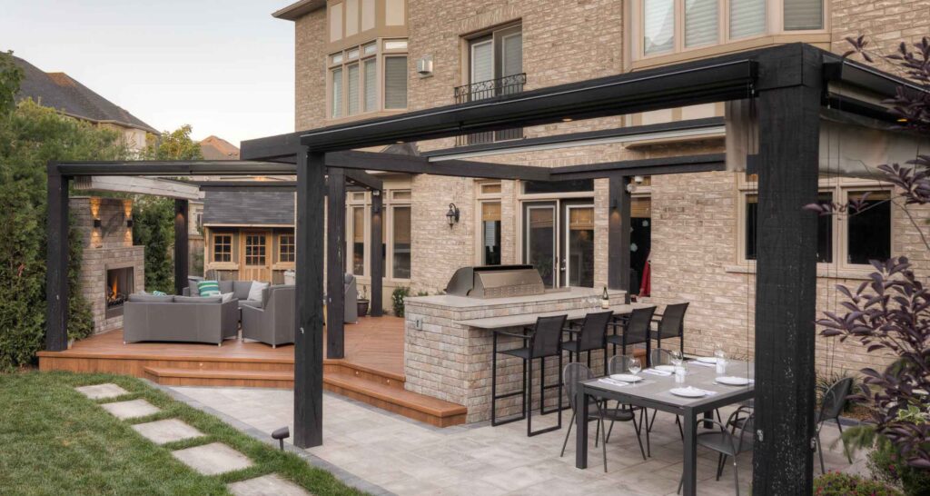 Backyard combining a deck and stone patio with an outdoor kitchen and pergolas for shade