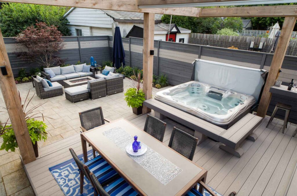 Downtown backyard with a deck featuring a dining area, hot tub, and lower stone patio for relaxation