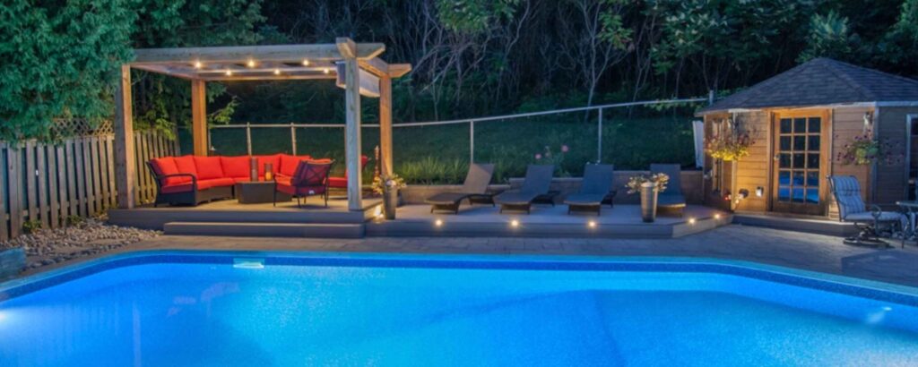 Nighttime pool with landscape lighting and a deck for relaxing evening enjoyment