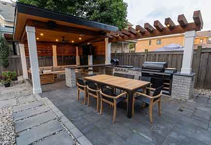 Outdoor kitchen with pergola, cabana lounge with TV, wellness area, and greenery lighting in a luxury backyard