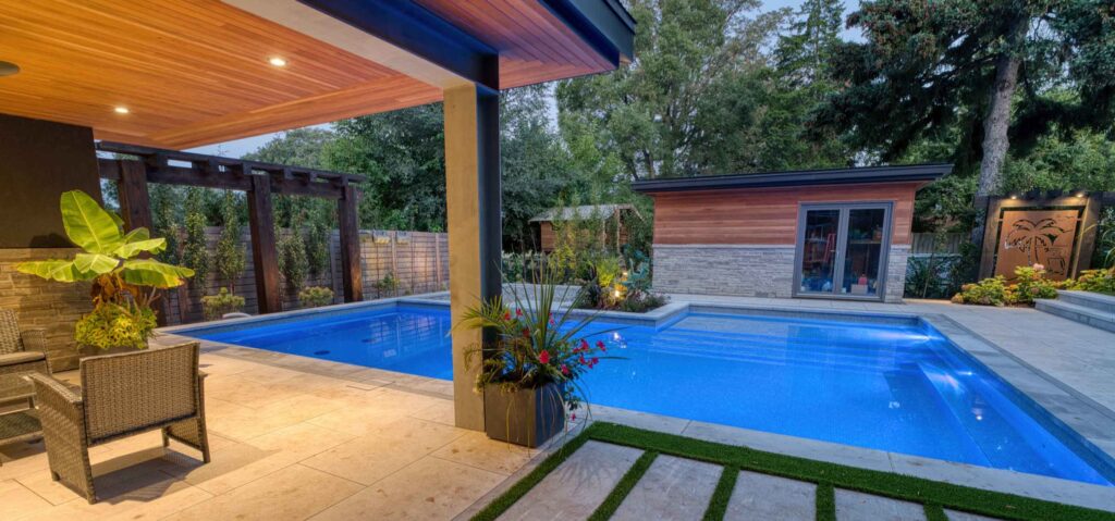 Contemporary L-shaped pool with a custom roofed seating area and lush planting for a green backyard feel