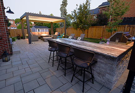 One-level backyard in Mississauga with Techo-Bloc patio, outdoor kitchen with privacy screen, louvered pergola seating area, and hot tub corner with garden lighting.