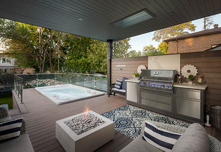 Modern downtown Toronto backyard with Wolf PVC deck, roof overhang, swim spa with glass railings, outdoor kitchen, fire table, turf lounge area, and cedar shed.