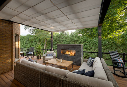 Modern Mississauga backyard featuring a single-level PVC deck, timber pergola with retractable awning, outdoor kitchen under a sloped roof, and a stone firepit seating area.