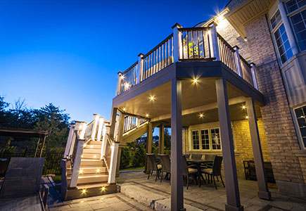 Elevated second-floor deck in Brampton with ravine view seating, illuminated stairs, and covered dining space overlooking the pool.