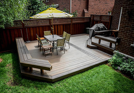 Two-level Trex composite deck in Oakville with built-in benches, angular layout, BBQ and dining area, and a long-lasting Ipe hardwood fence.