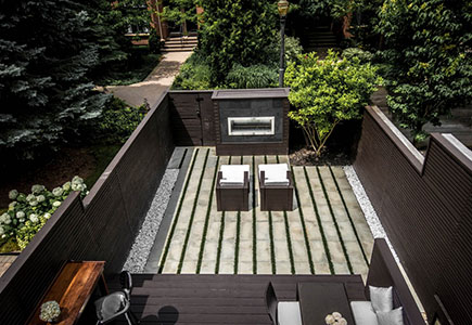 Modern Toronto backyard featuring a deck, horizontal privacy fence, linear stone and turf layout, and a stone-and-wood fireplace focal point.
