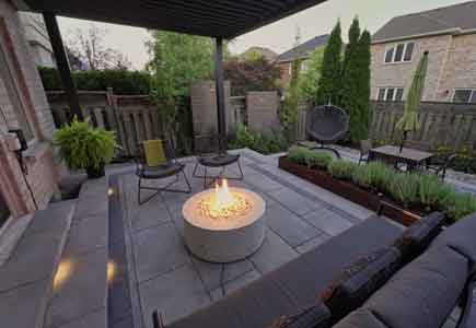 Multi-level backyard with louvered pergola, firepit lounge, dining area, stone patio, corten planter, and privacy screens in Oakville townhome
